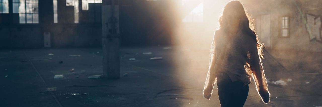 photo of woman walking in empty warehouse silhouetted by sunlight