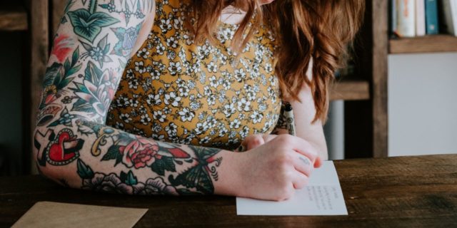 photo of redhead woman with tattoos writing a letter