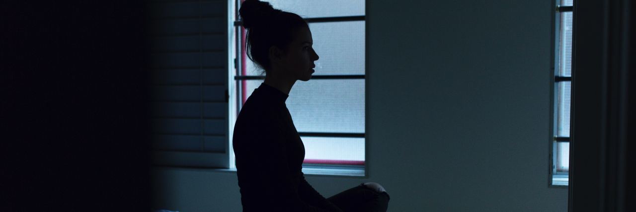 When Depression Makes You Feel Like a Zombie silhouette of a woman sitting cross-legged on her bed staring off into space