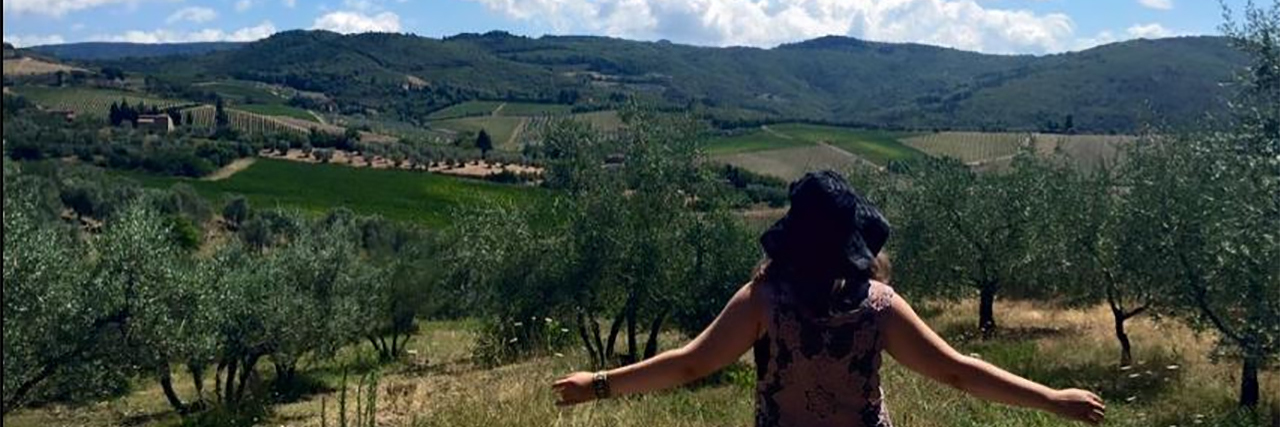 Radical Self-Acceptance and Self-Love When You Have Anxiety photo of contributor standing with back to camera looking out over fields and trees, arms stretched open, with a blue sky overhead