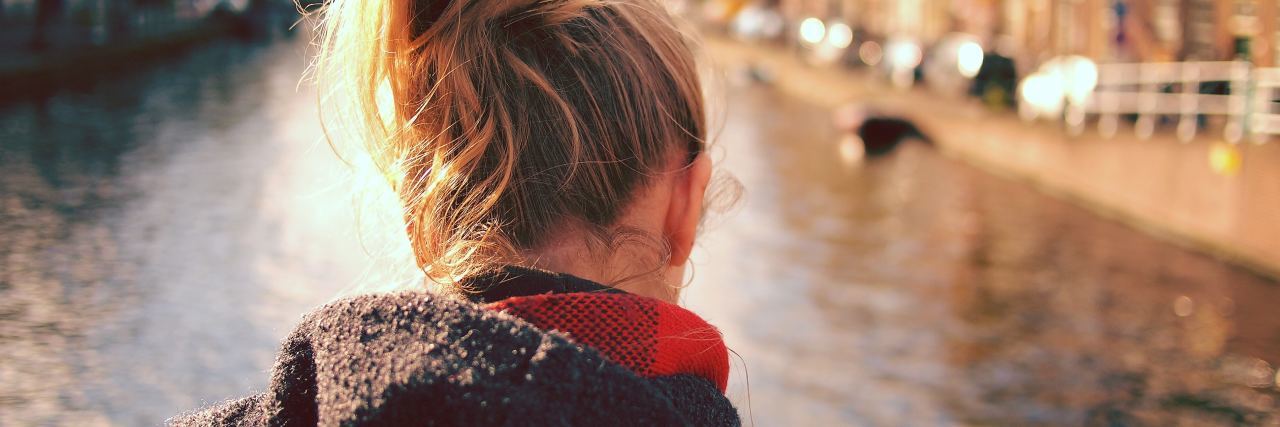 Types of Negative Thinking in Mental Illness close up photo from behind of woman looking down at canal or river as if in thought