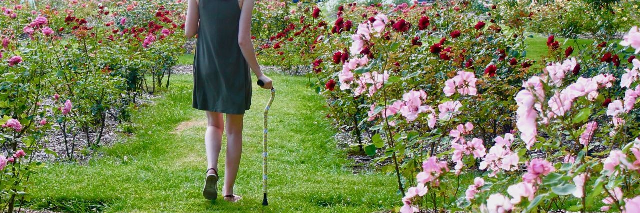 Accepting Your Need to Use Mobility Devices April walking wihth her cane in a flower garden.