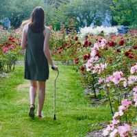 April walking wihth her cane in a flower garden.