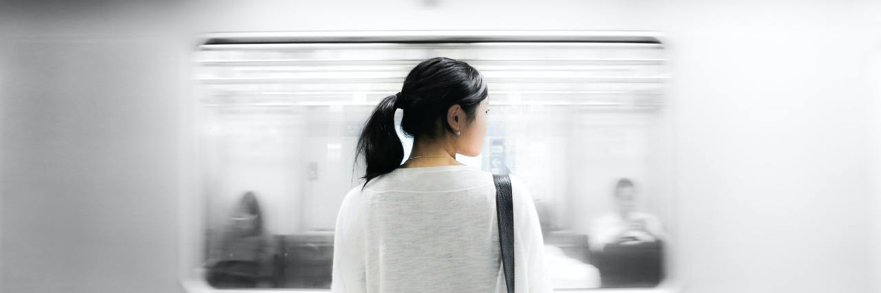 Woman staring with a train passing in the background with her hair up in a ponytail in muted colors