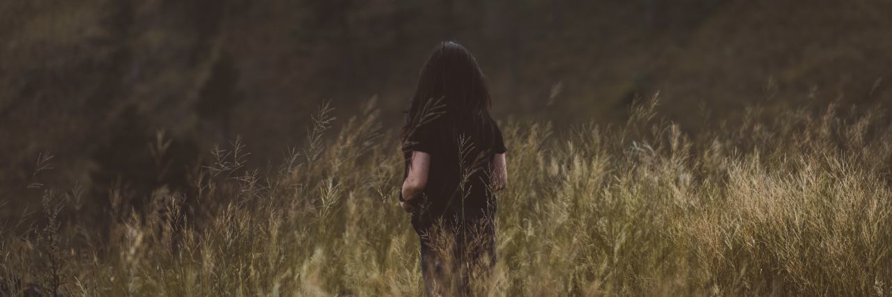 photo of dark haired woman from behind standing in long grass