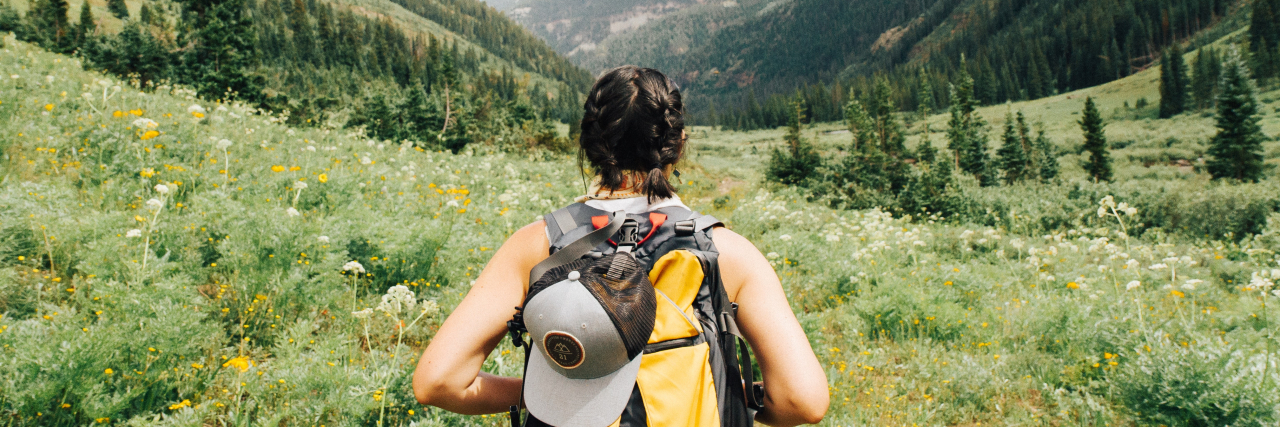 photo of a woman hiking through a field and mountains in the distance