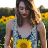 photo of woman standing in field of sunflowers looking down with one in her hand