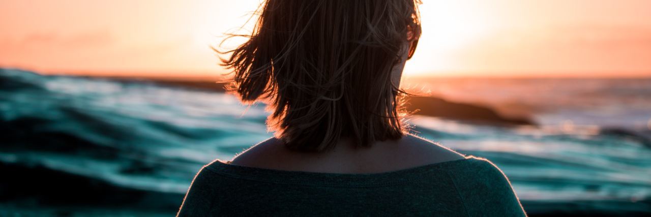 My Creativity Is a Gift From Borderline Personality Disorder photo of woman standing in front of ocean at sunset silhouetted by the light and facing away