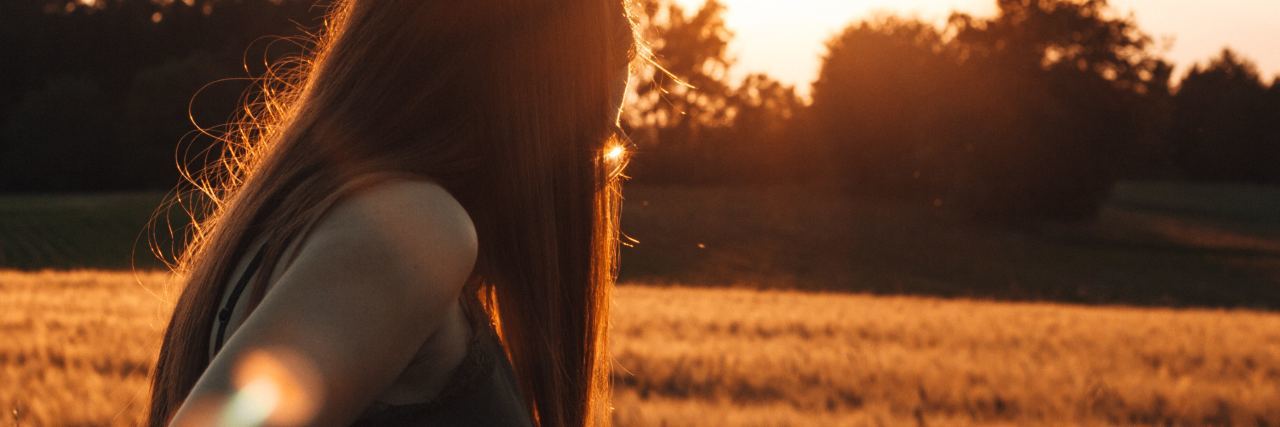 photo of woman standing in sunny sunset field looking happy