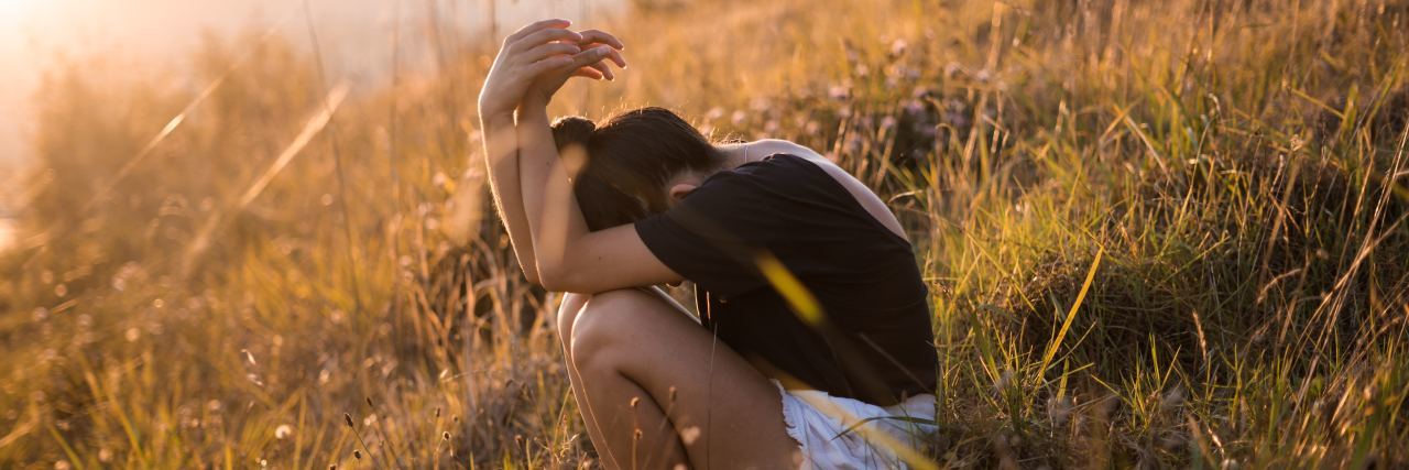 photo of woman sitting on grassy hillside with face buried in arms