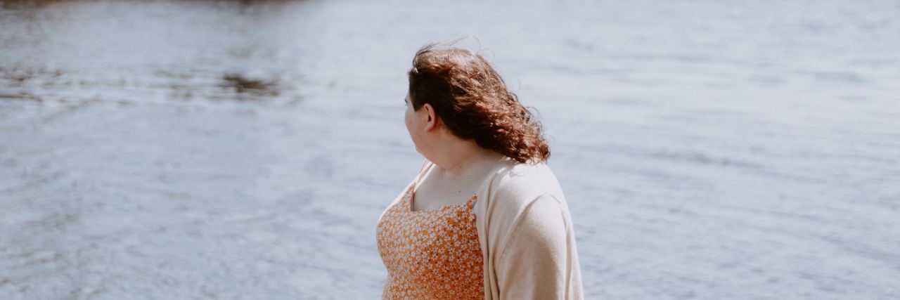 photo of woman standing by lake looking away from camera toward water