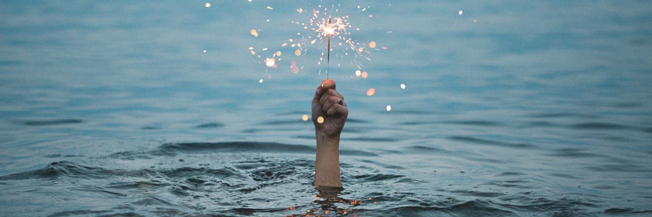 photo of hand rising out of ocean holding a sparkler