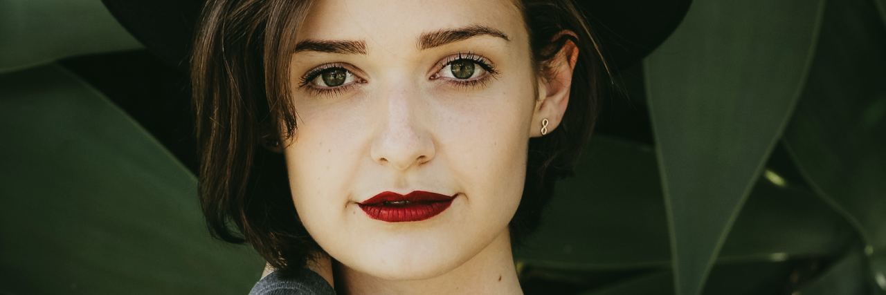 Radical Acceptance in Borderline Personality Disorder Recovery photo of young woman with black hat standing in front of leaves and looking into camera