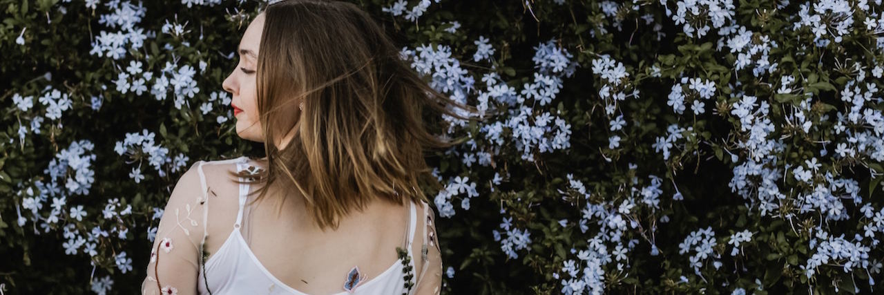 A woman in a white dress in front of a bush filled with flowers