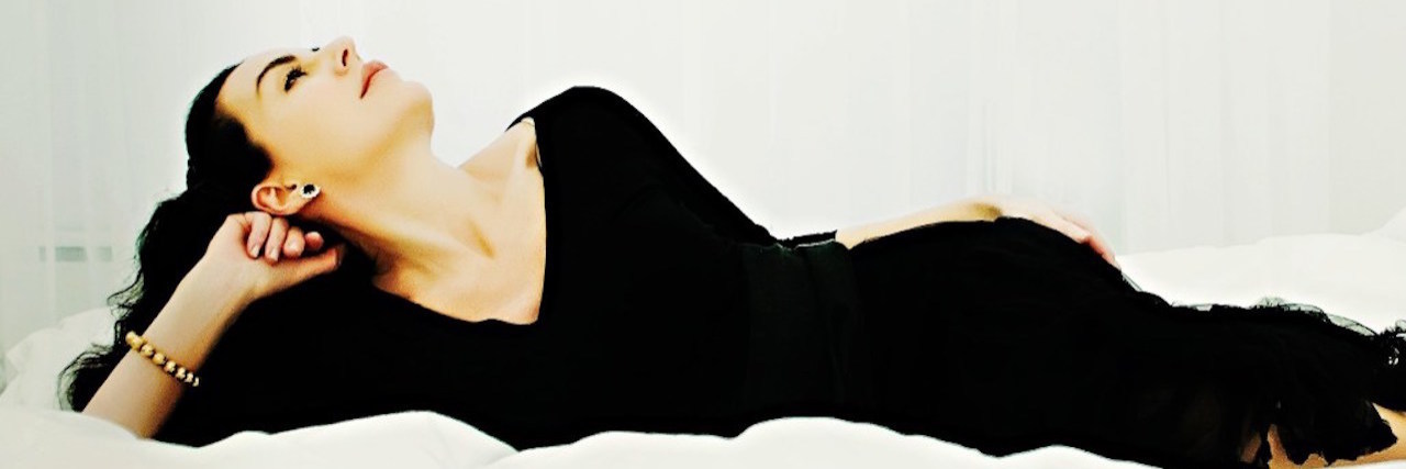 woman in a black dress lying on a white bed against a white background