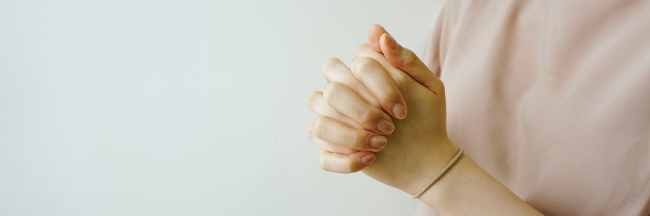 close up photo of woman's hands clasped in prayer against pale white background or wall
