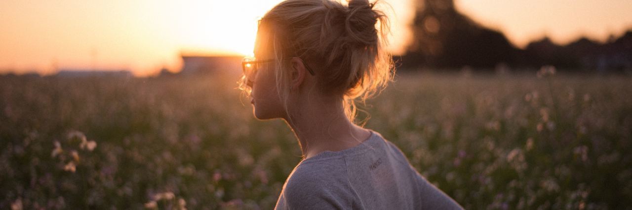 photo of woman with glasses standing in field at sunset