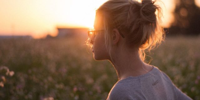 photo of woman with glasses standing in field at sunset