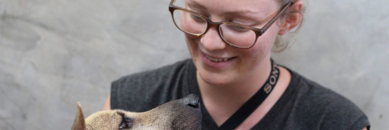 woman wearing glasses and smiling down at a dog