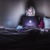A woman sitting in a dark room looking at her laptop, which is glowing
