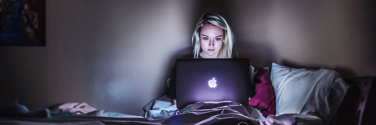 A woman sitting in a dark room looking at her laptop, which is glowing