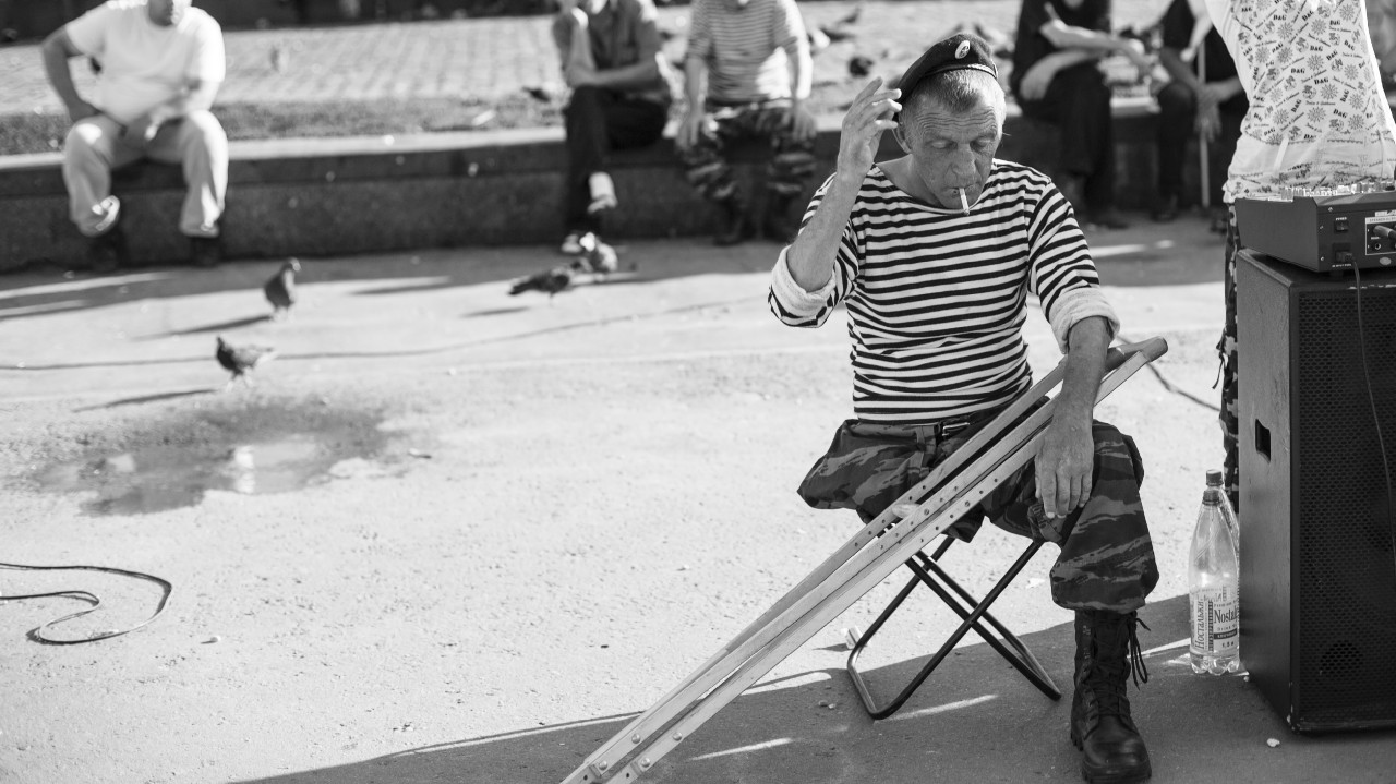 Man with leg amputation sitting on a stool outdoors.