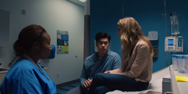 Chloe sits on an exam table. Zach and a doctor are also in the room.