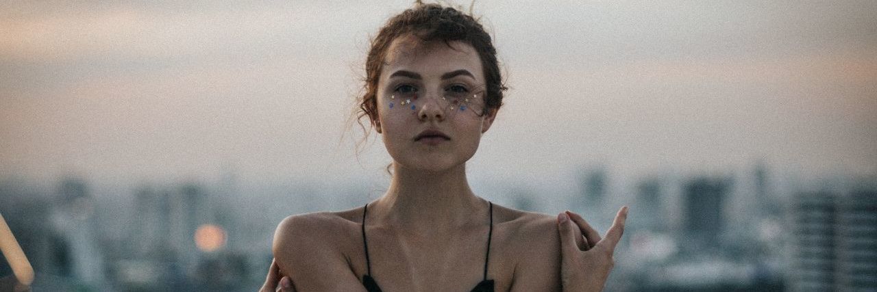 Advice People With Chronic Illness Would Give to Those Just Diagnosed woman with sparkles under eyes posing with arms in front of chest