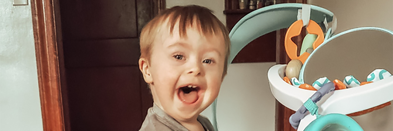Shannon's son, a small boy with Down syndrome, blonde hair and a big smile, playing at home.