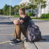 Boy sitting on the curb in front of his school looking away from camera