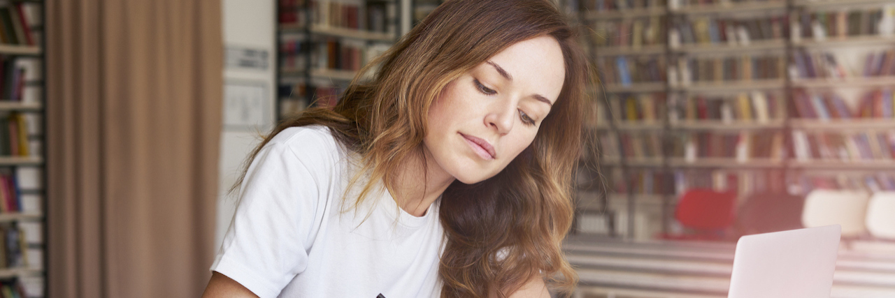 Should People With Mental Illnesses Be Social Workers? A woman writing in a notebook in front of her laptop at a library, studying