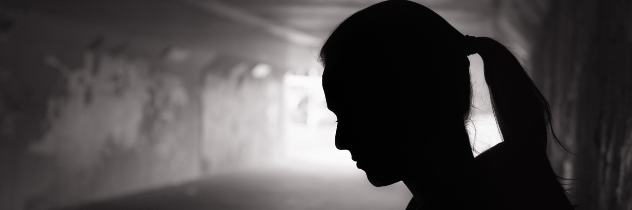 Letter to a Friend Who Blamed Me for Being Abused A woman stands with her head bowed in a dark tunnel.