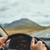 focus on someone's hands on the wheel of a car, with a wide open road
