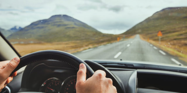 The Toll of Traveling Hundreds of Miles for Treatment Because I'm Rare focus on someone's hands on the wheel of a car, with a wide open road