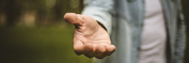 Young man in standing in park stretches his hand. Focus is on hand. Close up.