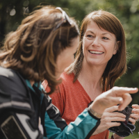 Small group of mature female cyclists sitting down in the outside seating area of a cafe. Tey are enjoying some refreshments as they take a break.