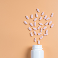 Pink pills, tablets and white bottle on yellow background.