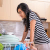 woman standing in front of full kitchen sink, looking tired