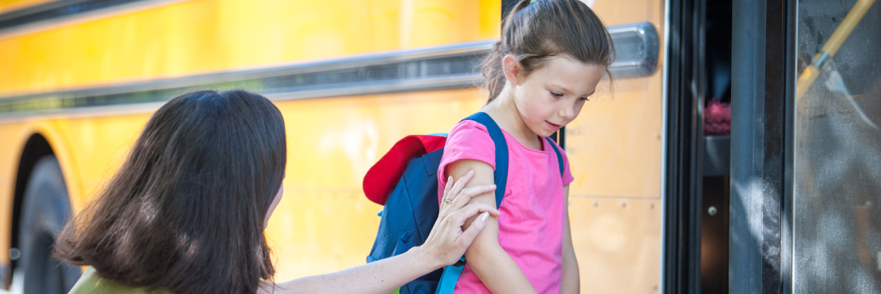 Girl sad and being comforted as she gets on the school bus.