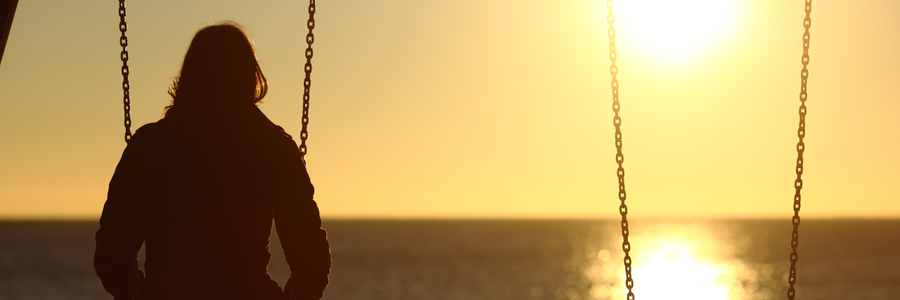 What to Remember About Grieving a Breakup woman on a swing with her back toward the camera looking into a sunset over the beach with another empty swing next to her