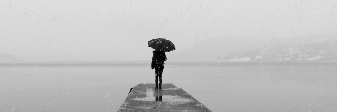 Living With Chronic Illness: Deciding Whether to Reach Acceptance woman standing with umbrella at the end of a dock near the water.