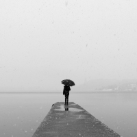 woman standing with umbrella at the end of a dock near the water.