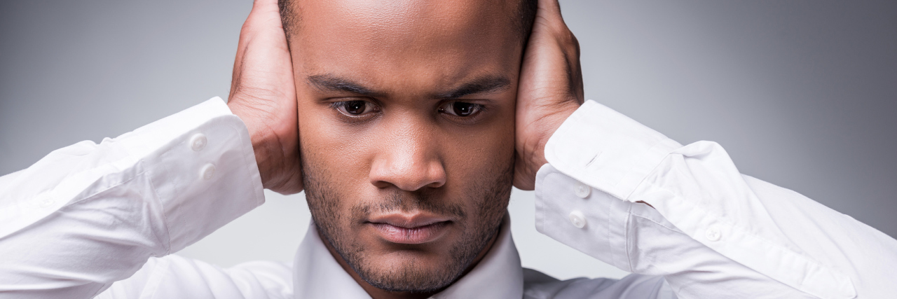 What Triggers Autistic Meltdowns? A distressed man in business clothes, covering his ears.