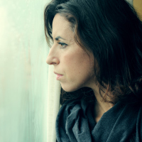 A woman stands and intensely stares out of a window.