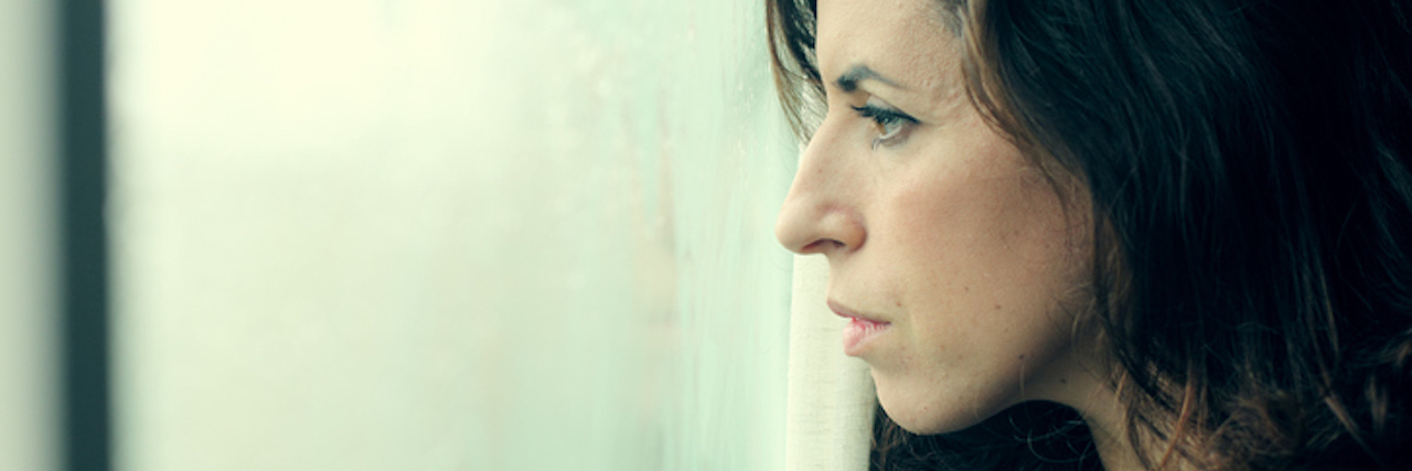 What You Should Know About Chronic Illness-Induced PTSD beautiful 35 year old woman stands in front of the window