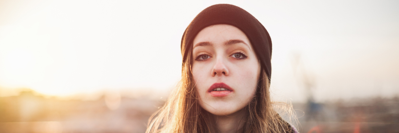 Struggling With Mental Illnesses and learning disabilities A woman stands outdoors in front of a sunset.
