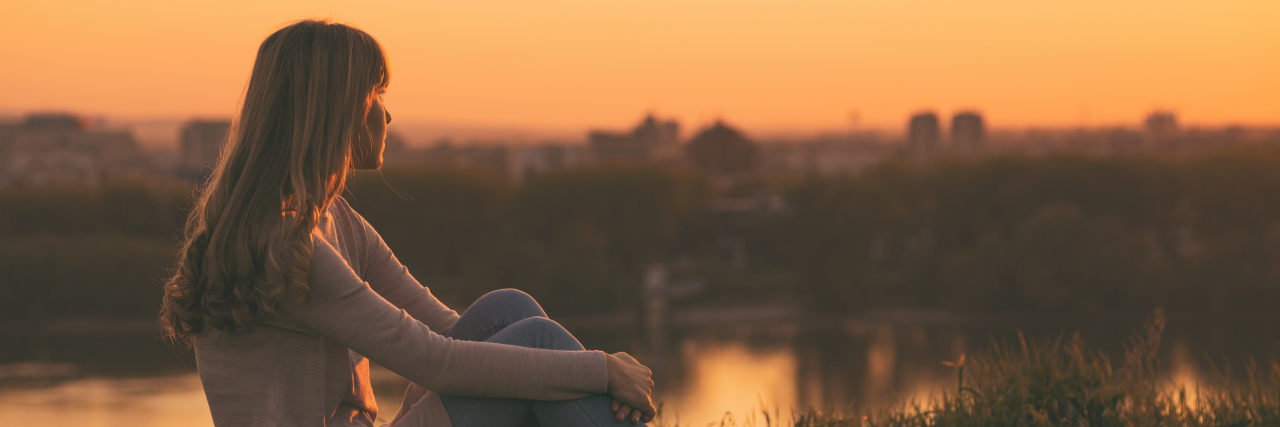 How the Mind Works When Grieving a Loved One a woman is sitting watching the sunset