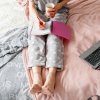 woman in pajamas in bed with a computer and notebook
