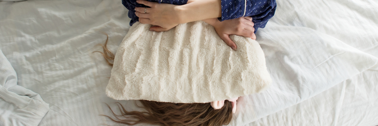 Dealing With Chronic Illness and Society's Expectations woman laying in bed, tired, with a pillow over her face