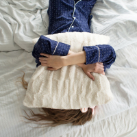 woman laying in bed, tired, with a pillow over her face